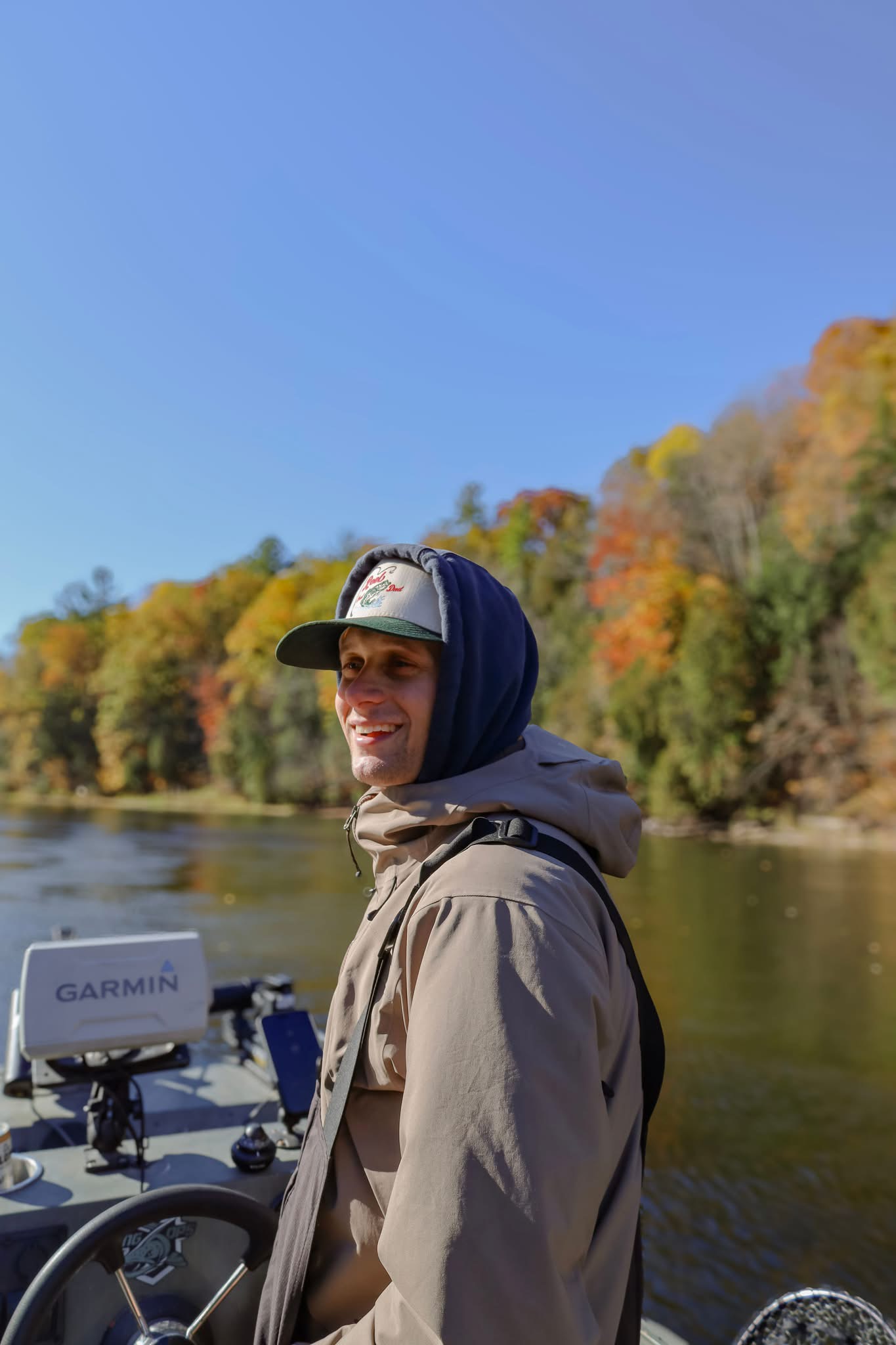 Captain Spencer Behler smiling aboard his fishing boat on a Michigan river in autumn